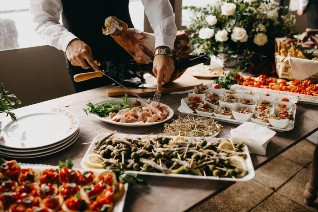 pexels-photo-2814828-2814828 A chef slices meat in a beautifully arranged catering setup with diverse appetizing dishes.